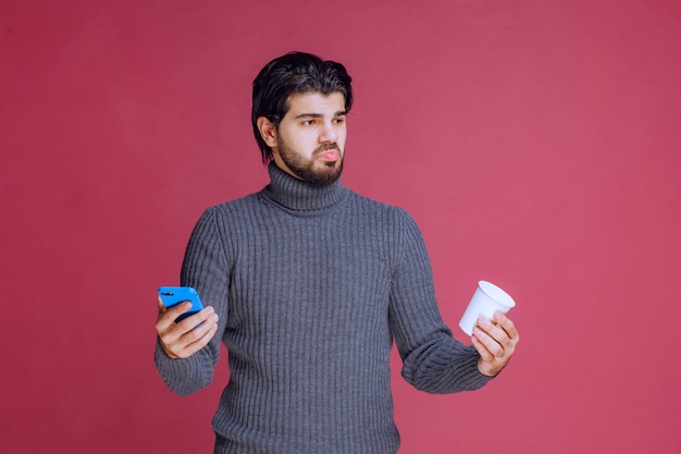 Man holding a smartphone and a coffee cup and looks confused.