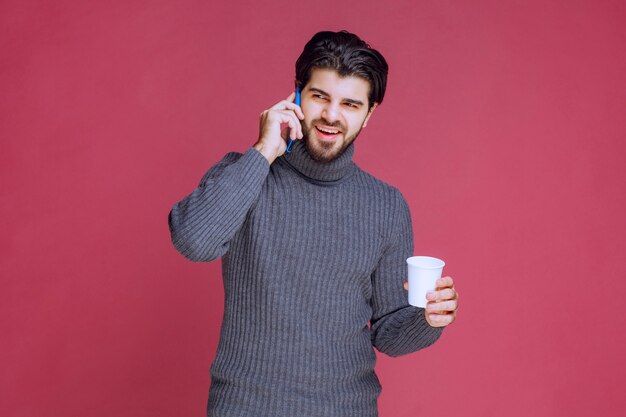 Man holding a smartphone and a coffee cup and talking.