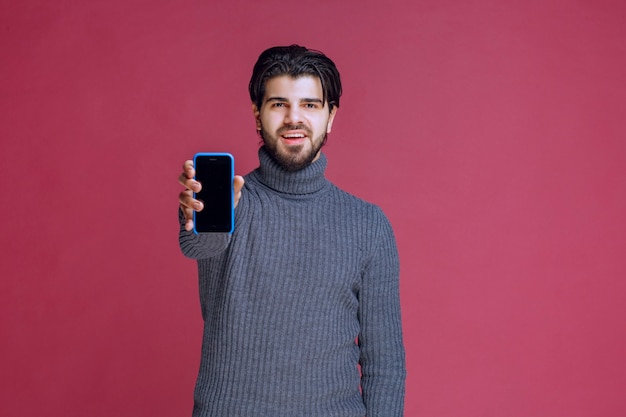 Free photo man holding a smartphone and presenting it to the customers.