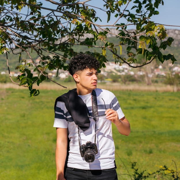 Man holding spectacle with camera around his neck looking away