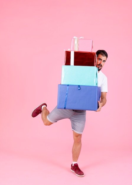 Man holding stack of gift boxes running against pink background