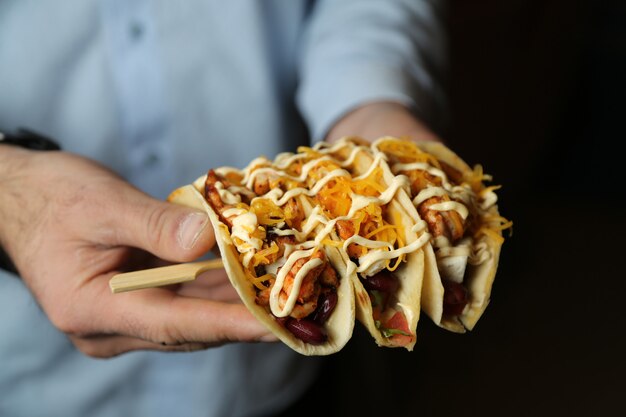 Man holding sticks with tacos chicken beans tomato pepper cheese