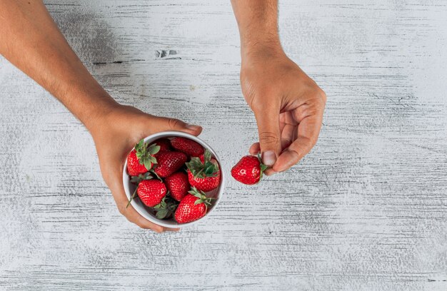 Man holding strawberries in a bowl and hand top view on a light wooden background space for text