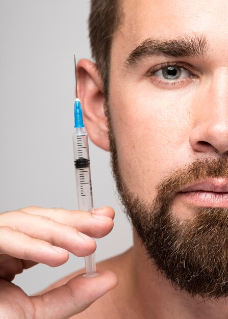 Man holding a syringe next to his face close-up