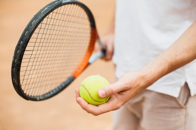 Мужчина держит теннисный мяч и ракетку