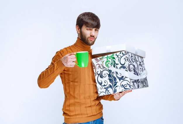 Man holding a white blue gift box and having a green cup of satisfaction coffee.