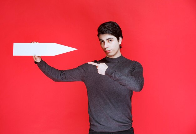 Man holding a white direction arrow pointing at himself