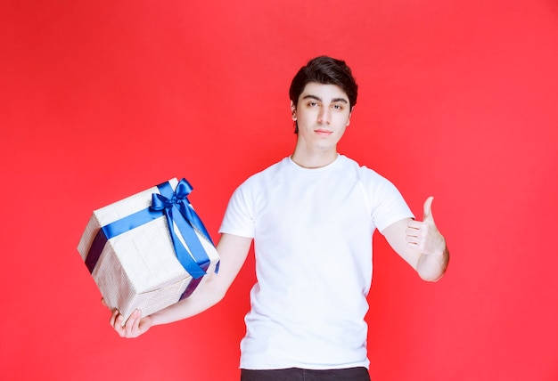 Мужчина держит белую подарочную коробку и показывает положительный знак рукой