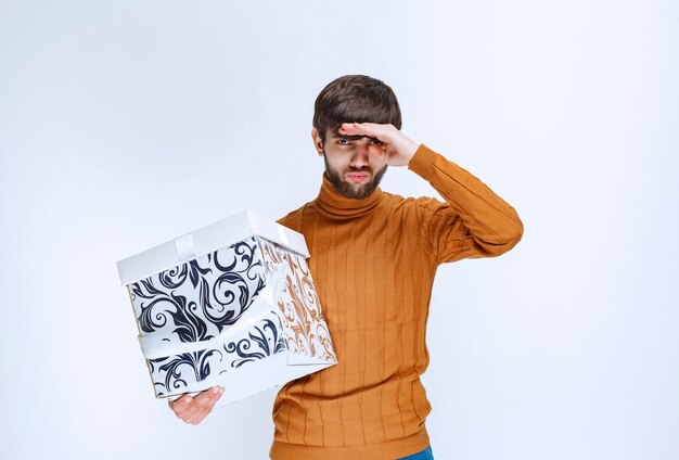 사람을 알아 채기 위해 소리를내는 파란색 패턴의 흰색 선물 상자를 들고있는 남자.