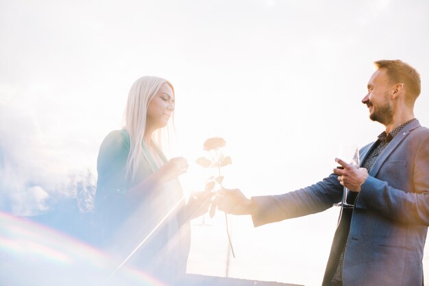 Man holding wineglass giving rose to her girlfriend in bright sunlight