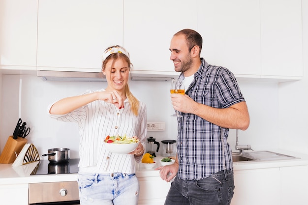 Мужчина держит бокал в руке, глядя на ее улыбается женщина, приправляя соль в салат