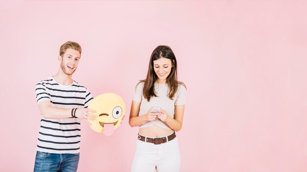 Man holding winking eye emoji near smiling woman using cellphone