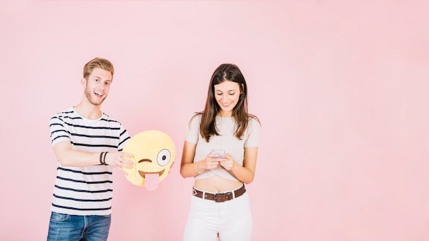 Man holding winking eye emoji near smiling woman using cellphone