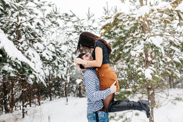 Man holding woman in arms in winter forest 