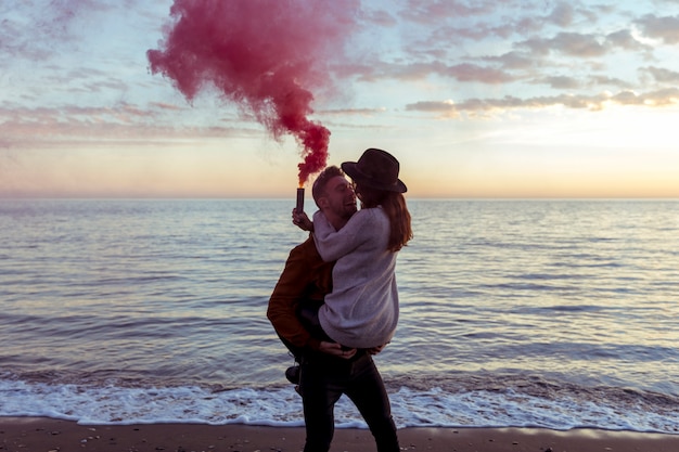 Мужчина держит женщину в руках с дымовой шашкой на берегу моря
