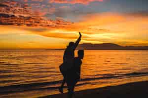 Free photo man holding woman on back on evening sea shore