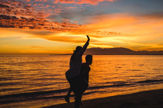 Man holding woman on back on evening sea shore