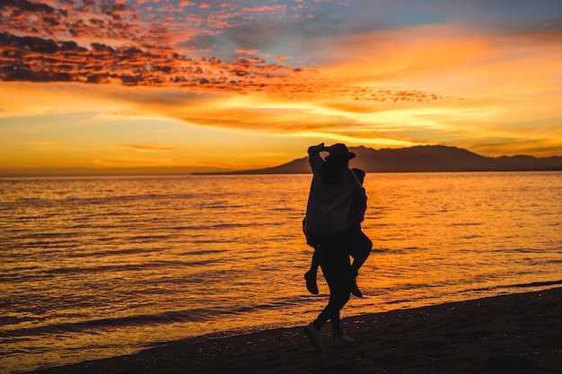 Мужчина держит женщину на спине на берегу моря ночью