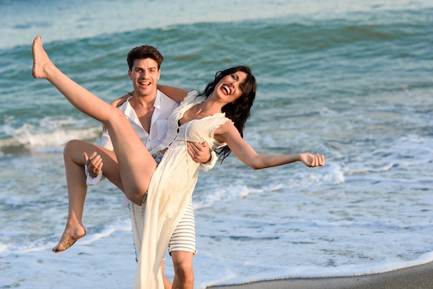 Free photo man holding a woman in white dress on the beach