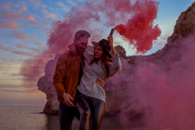 Man holding woman with pink smoke bomb on sea shore 