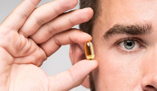 Man holding an yellow pill next to his face