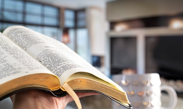 Free photo a man holds a bible against the background of the living room. reading a book in a cozy atmosphere. close up.