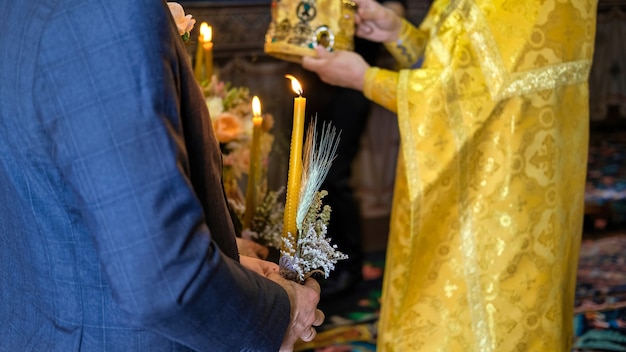 Мужчина держит свечу, православный священник служит в церкви. Свадебная церемония