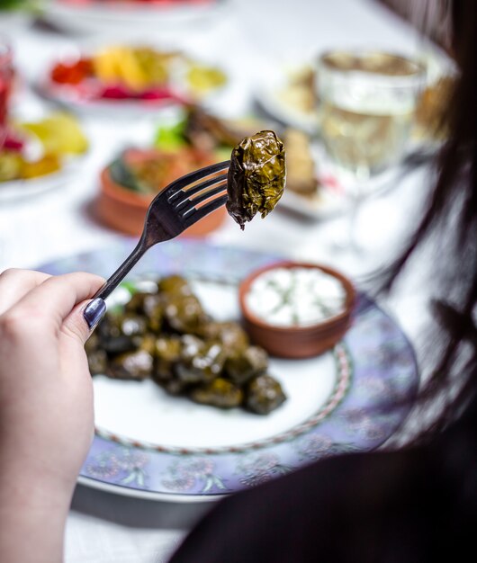 Man holds fork with grape leaves dolma plain youghurt side view