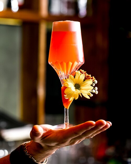 Man holds a glass of orange cocktail garnished with flower