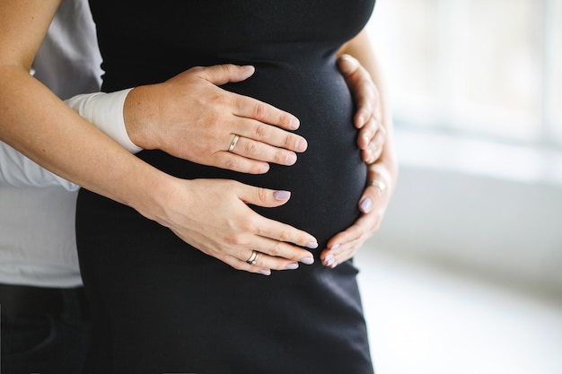 Man holds hands for her pregnant wife belly, side view