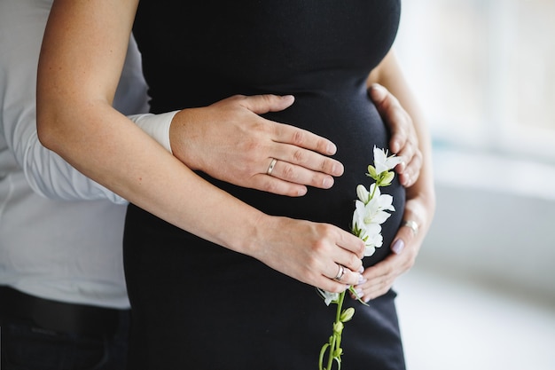 Man holds hands for her pregnant wife belly, and woman holds a white flower