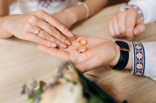 男は彼の腕の上に女性の前に2つの金の結婚指輪を保持する