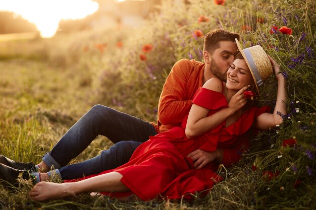 남자는 빨간 양 귀 비와 함께 녹색 잔디밭에 그녀와 함께 앉아 그의 여자 부드러운 보유