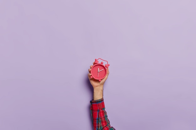 man holds little red alarm clock in hand