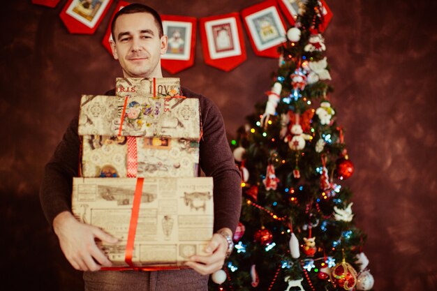 man holds a lot of gifts near a Christmas tree.