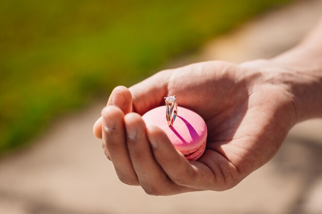 Man holds pink macaroon with wedding ring