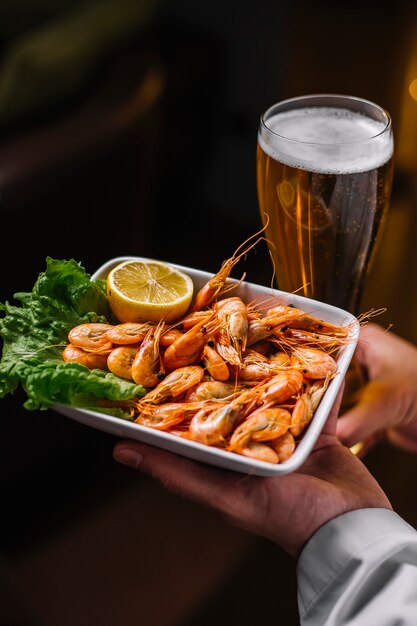 Man holds the plate with shrimps on lettuce lemon side view