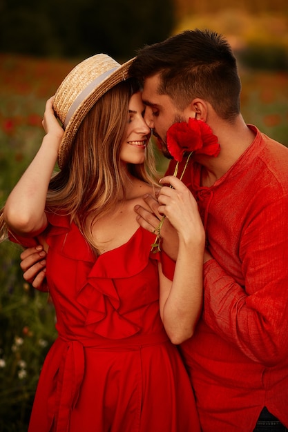 Man holds tender beautiful woman standing with her on the green field with red poppies