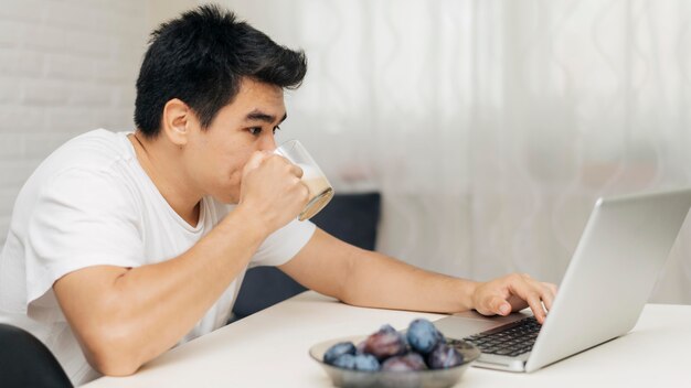Uomo a casa durante la pandemia utilizzando laptop e prendendo un caffè