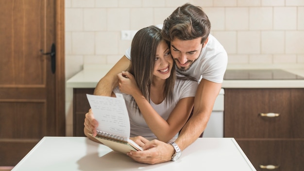 Man hugging cheerful girlfriend with notebook