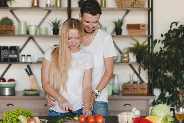 キッチンカウンターで野菜を切る彼女のガールフレンドを抱き締める男