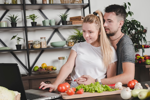 Man hugging her girlfriend using laptop white preparing food