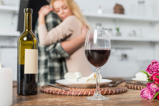 Мужчина обнимает женщину возле стола с бутылкой и бокалом вина