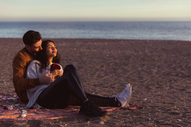 Man hugging woman on coverlet on sea shore 