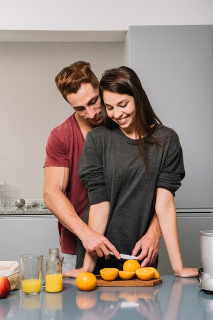 Man hugging woman from behind and cutting orange