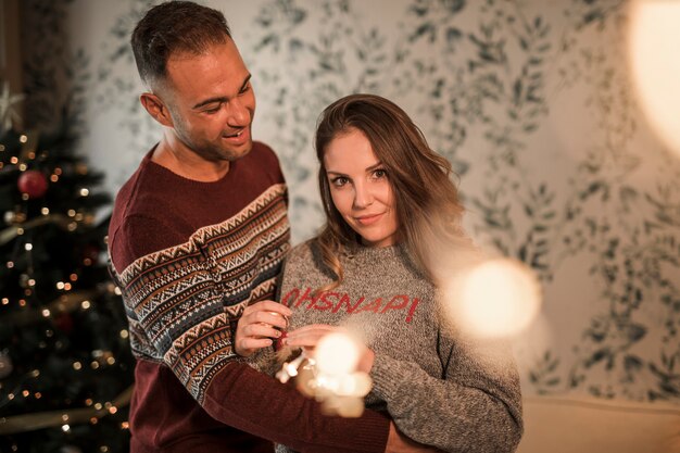 Man hugging woman in sweaters near Christmas tree