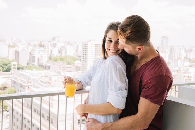Мужчина обнимает женщину со стаканом сока на балконе