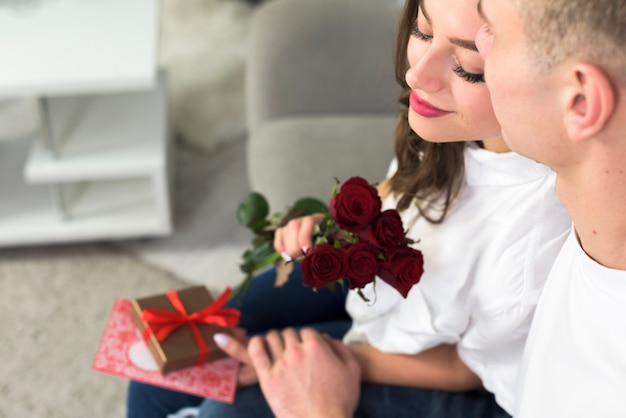 Man hugging woman with red flowers on couch