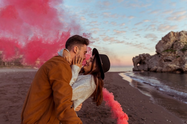 Бесплатное фото Мужчина обнимает женщину с дымовой шашкой на берегу моря