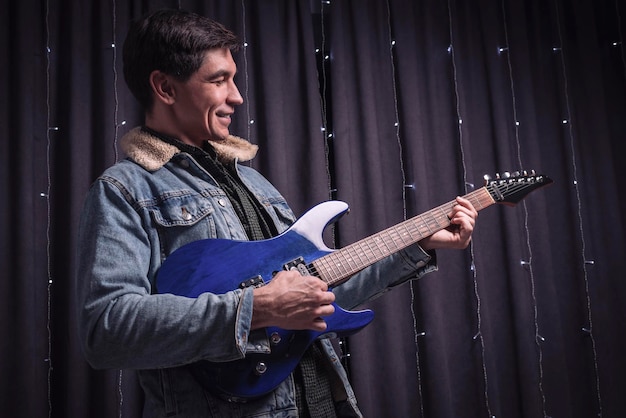 데님 재킷을 입은 남자가 파란색 일렉트릭 기타를 연주합니다. 콘서트 개념입니다. 혼합 매체